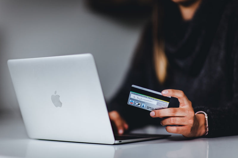 woman looking at a macbook with a card on her hands